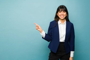 Gorgeous hispanic woman in her 20s smiling looking professional wearing a business suit pointing to copy space