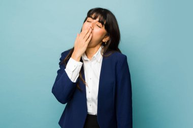 Tired latin young woman yawning and feeling sleepy while looking exhausted because of her professional work