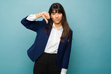 Disappointed young woman looking upset and sad while doing a thumbs down feeling frustrated