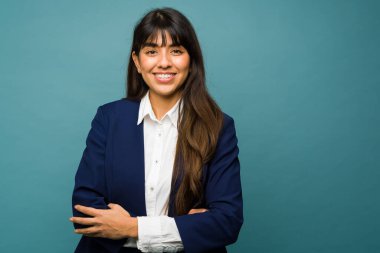 Attractive young woman smiling making eye contact while wearing a professional business suit against a blue background with copy space
