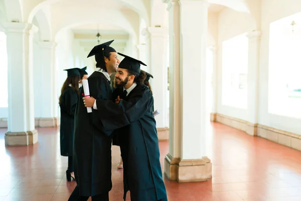 Веселые Мужчины Латиноамериканские Друзья Обнимаются Празднуют После Получения Университетских Дипломов — стоковое фото