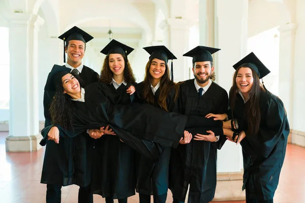 Attractive Friends Having Fun Wearing Graduation Gowns While Carrying Friend — Stok fotoğraf