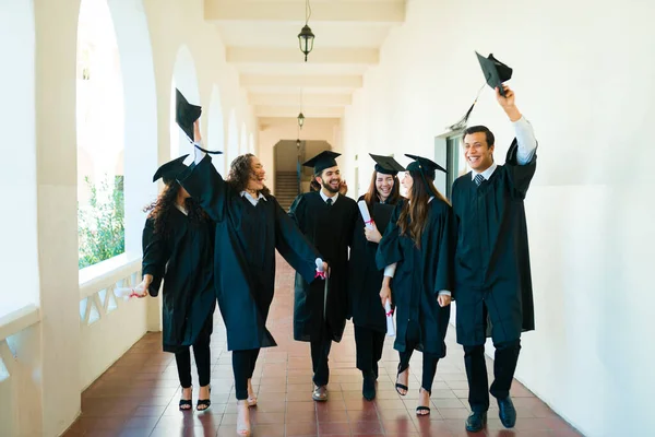 Happy Graduates Walking Together College Hall Wearing Graduation Gowns Talking — Fotografia de Stock