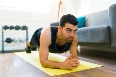 Determined latin man doing plank exercises and working out with motivation in his living room home