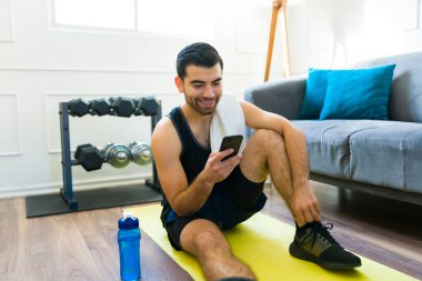 Cheerful active man texting on his phone and smiling while ready to start his fitness workout at his home gym
