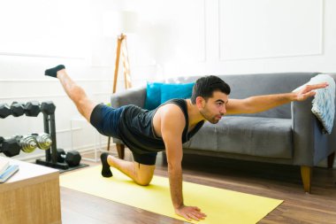 Attractive hispanic man exercising and doing a workout routine at his home gym in the living room