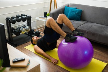 Active hispanic young man using a stability ball for his home workout exercises in the living room