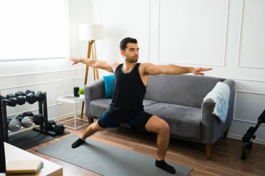 Sporcu Latin bir adam evde yoga egzersizi yaparken savaşçı pozu veriyor.