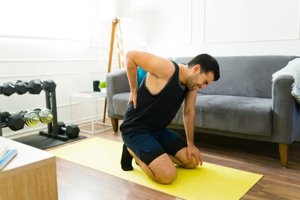 Stressed fit man suffering a back injury while doing workout exercises in the living room