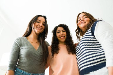 Low angle of beautiful women best friends hugging and smiling looking at the camera while hanging out together