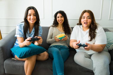 Güzel genç kadınlar ve pijamalı en iyi arkadaşlar pijama partisinde video oyunları oynayarak eğleniyorlar.