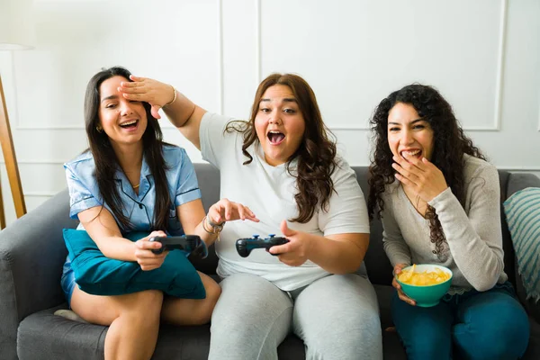 在一个睡梦中派对上 三位女性朋友一起玩电子游戏时 开心地大笑着 这令她们兴奋不已 — 图库照片