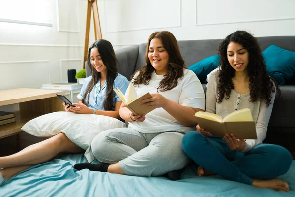 Happy relaxed women friends having a relaxing time during a slumber party while reading a book together