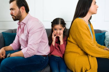 Çocuk velayeti ve boşanma konusunda tartıştıktan sonra kızgın ailesinin ortasında oturan korkmuş, üzgün, küçük bir kız.