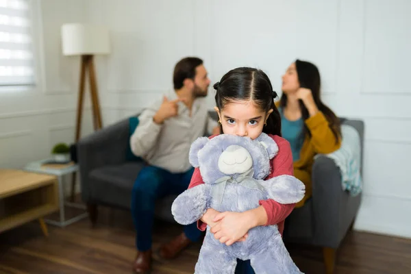 可爱的小女孩抱着一只泰迪熊 听着父母在客厅里吵架 看起来既害怕又伤心 — 图库照片