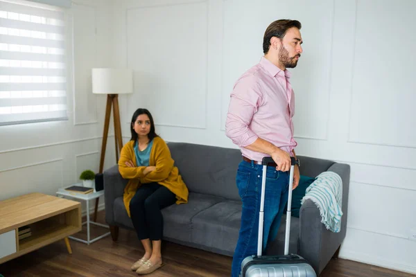 Annoyed upset man with a suitcase moving and leaving his wife after splitting up and having a divorce