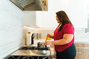 Aşırı kilolu şişman bir kadının güzel mutfağında yemek pişirirken mutlu görünmesi. 