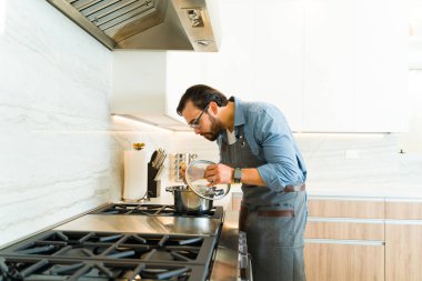 30 'lu yaşlarında beyaz bir adam ocakta yemek pişiriyor ve güzel beyaz mutfağında yemek yemeye hazır.
