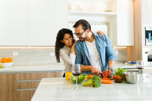 白い花崗岩のキッチン島で一緒に健康的なディナーを調理しながら 抱きしめる愛の笑みを浮かべてカップル — ストック写真
