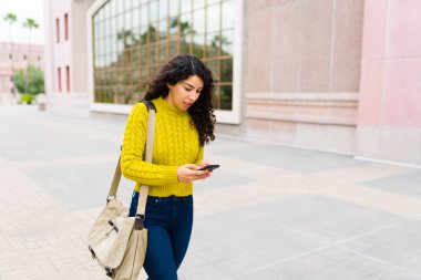 Güzel, beyaz bir kadın sabah işe giderken akıllı telefonuyla mesajlaşıp şehir caddesinde yürüyor.