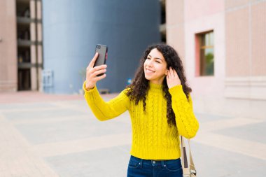 Neşeli beyaz kadın telefonuyla selfie çekiyor ve şehirde dolaşırken sosyal medya kullanıyor.