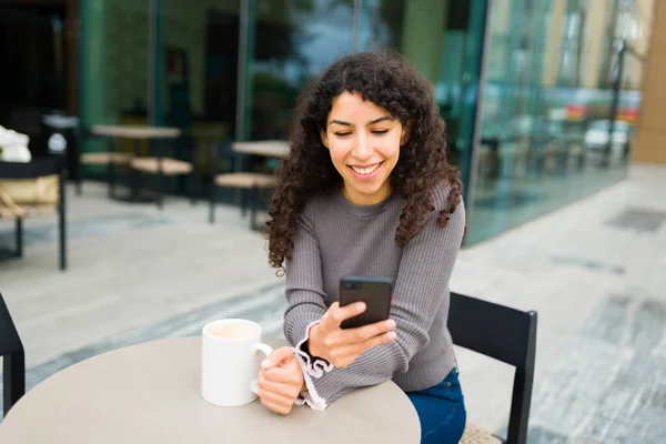 快乐的年轻女性一边微笑着一边用智能手机发短信 或者一边用社交媒体喝咖啡 — 图库照片