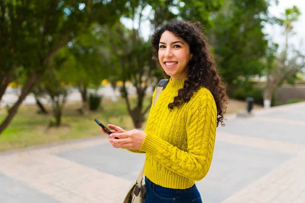 スマートフォンを使って街中を歩いていると 明るい若い女性がモバイル接続を使って文章を書く姿が描かれています — ストック写真