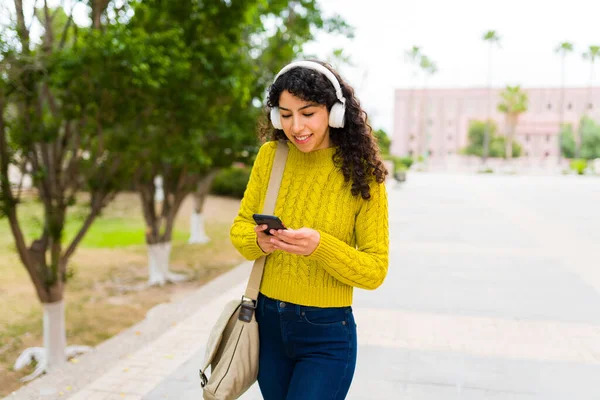 スマートフォンでテキストメッセージを送りながら通勤で仕事をしながら音楽を聴くヘッドフォンを持つ魅力的な幸せな女性 — ストック写真