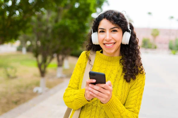 美しい白人女性はヘッドフォンで音楽を聞き 屋外でテキストメッセージを送信しながら 彼女の携帯電話を使用して — ストック写真