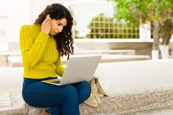 白种人年轻女性戴上耳机 一边在户外做远程工作 一边用笔记本电脑开始视频通话 — 图库照片
