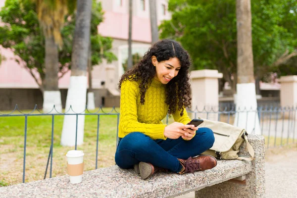 迷人的高加索女人放松地坐在公园的长椅上 一边微笑 一边用智能手机给朋友发短信 — 图库照片