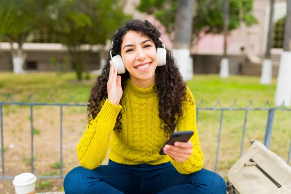 兴奋的年轻女性 戴着无线耳机 在户外用手机进行眼神交流和听快乐的音乐 — 图库照片