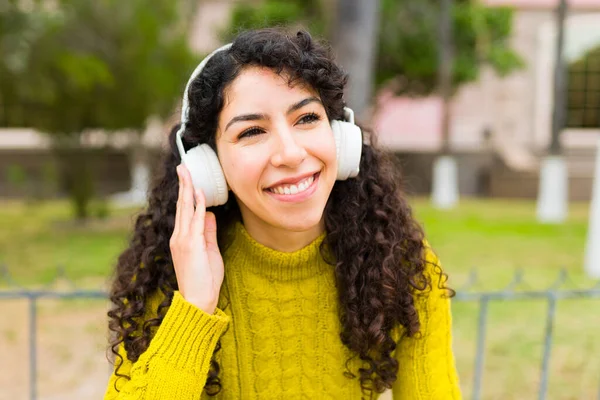 公園でワイヤレスヘッドフォンで音楽を聴きながら陽気に笑っているゴージャス若い女性 — ストック写真