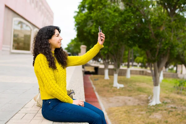 一位漂亮的年轻女子带着智能手机在户外自拍 在公园里的社交媒体上轻松地张贴自己的照片 — 图库照片