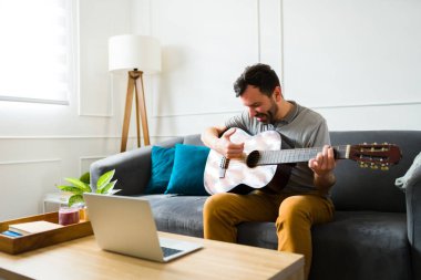 Evde dinlenirken gitar çalan ve müzik dinleyen yakışıklı bir adam.