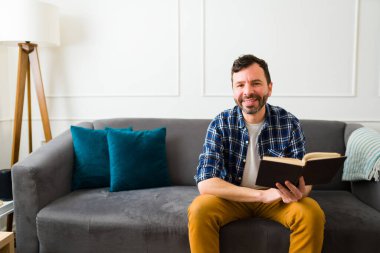 Evde boş zamanlarında kitap okumaktan zevk alan zeki çekici bir adam kameraya bakıyor.