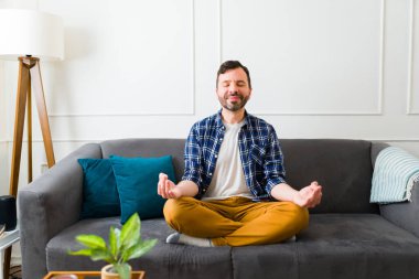 Rahatlamış, beyaz bir adam gülümseyerek kanepede oturup nefes egzersizi yaparken rahatlatıcı bir meditasyon yapıyor.