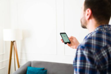 Beyaz adam arkadan hava durumu uygulamasını akıllı telefonundan kontrol ederken ya da evdeki klimayı açarken görülmüş.