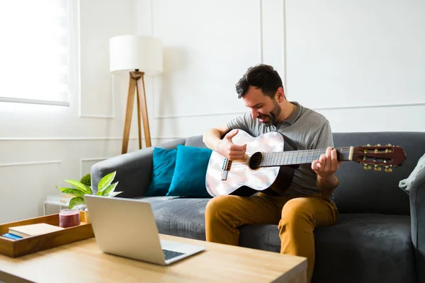 ギターを弾いたり 音楽を聴いたりしながら 余暇の間に家でリラックスしているハンサムな才能のある男 — ストック写真
