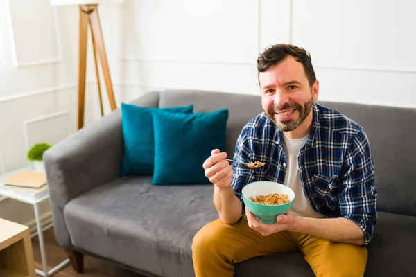30多岁的英俊而快乐的男人坐在沙发上吃麦片 在客厅里享受他的早晨 — 图库照片
