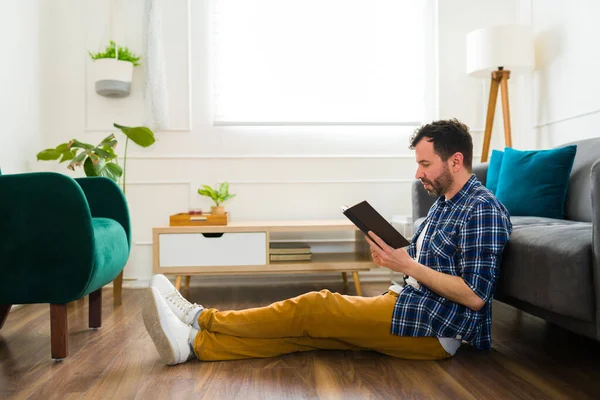 在客厅里一边欣赏一本好书 一边在家里休息的轻松的高加索人的侧视图 — 图库照片