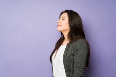 Güzel, genç bir kadın gözleri kapalı ve rahatlamış görünüyor. Fotokopi odası olan bir stüdyo arka planına yaslanıyor.
