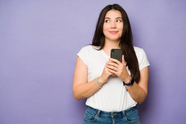 Mor arka planda fotokopi alanının yanında gülümserken akıllı telefonuyla mesaj atan ya da sosyal medya kullanan mutlu beyaz kadın.
