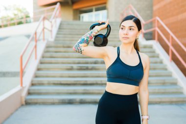 Çekici, spor giyimli genç bir kadın. Kettlebell ağırlığını kaldırıyor ve dışarıda çalışıyor.