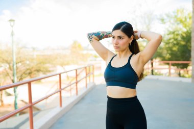 Aktif formda genç bir kadın saçını ve at kuyruğunu düzeltiyor ve dışarıda koşuya çıkmaya hazırlanıyor.