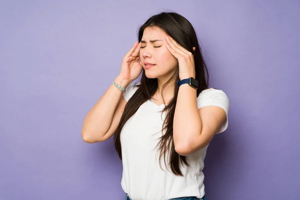 患有头痛或偏头痛的压力很大的年轻女性在紫色背景下感到身体不适 — 图库照片