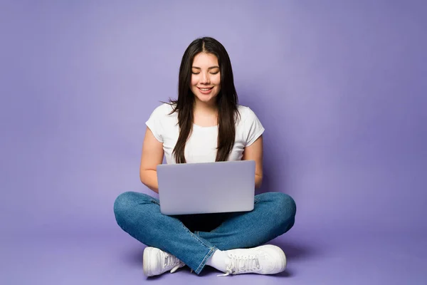 在紫色背景的笔记本电脑上打字时 穿着休闲装的快乐女人放松了下来 — 图库照片
