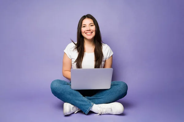 在紫色工作室使用笔记本电脑时 快乐的高加索女人一边微笑一边放松 一边眼神交流 — 图库照片