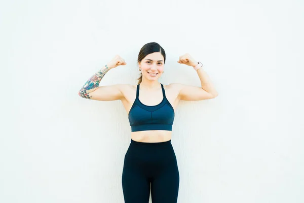 Portrait of a strong happy beautiful woman in her 20s with a tattoo arm doing bicep curls while working out