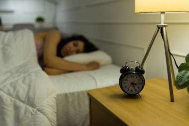 Yatakta uyumaya çalışan huzursuz genç bir kadının yanında alarmlı bir saatle bir gece standının ön planına odaklan.